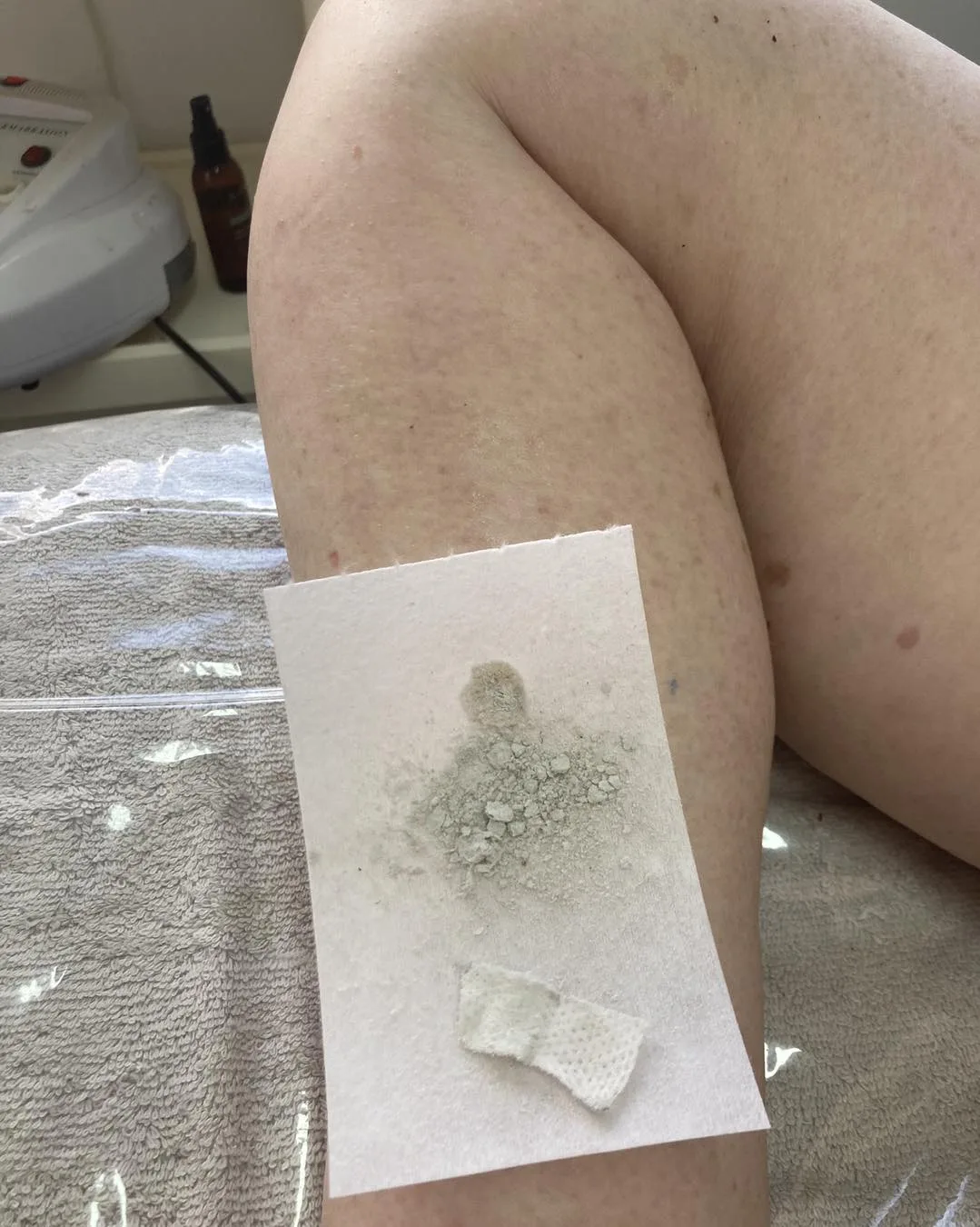 A wax strip laid across a shin with the lifted wax and hair visible — mid-session on a towelled bed