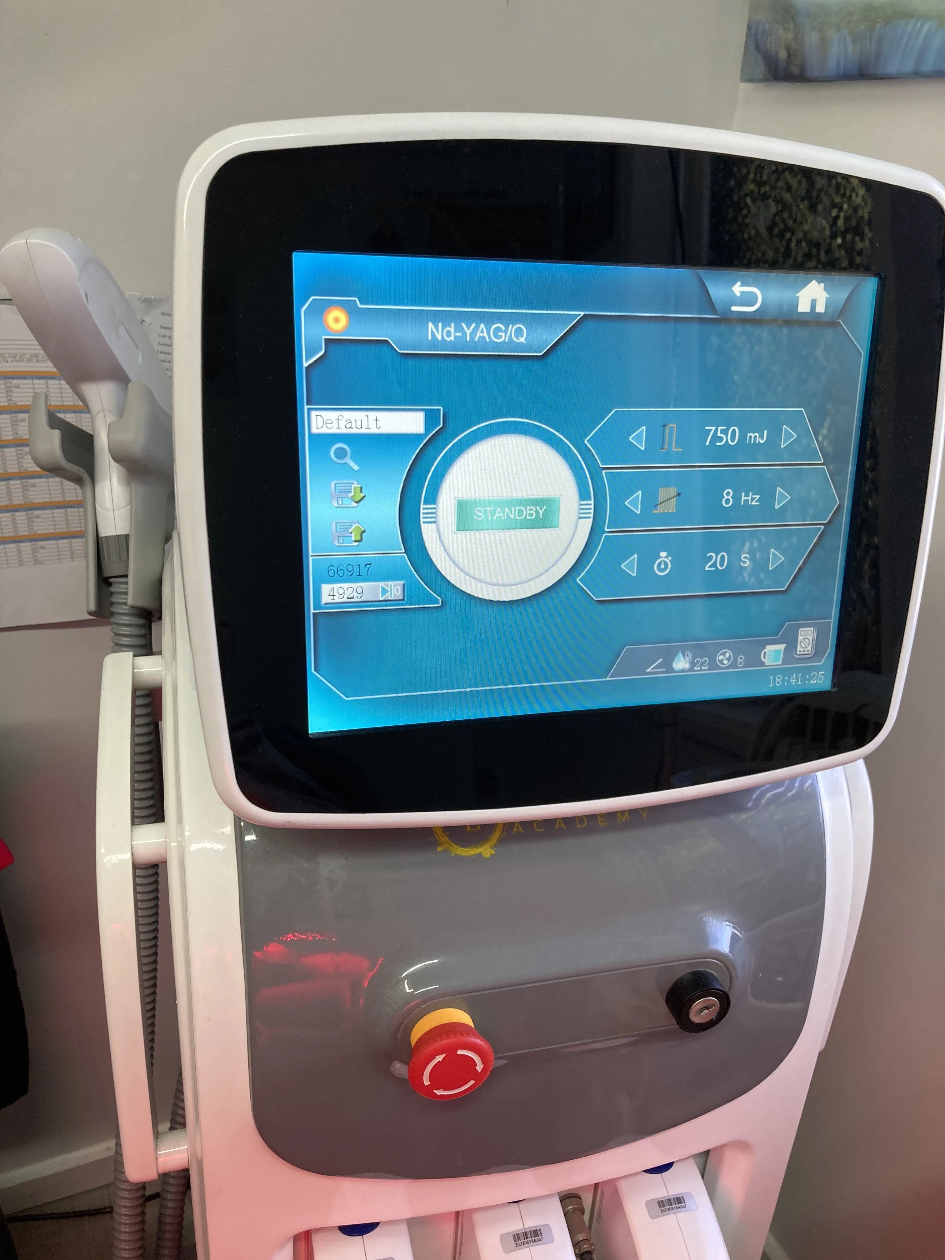 The Nd-YAG laser console in the treatment room — touchscreen showing 750 mJ / 8 Hz, three handpieces docked below